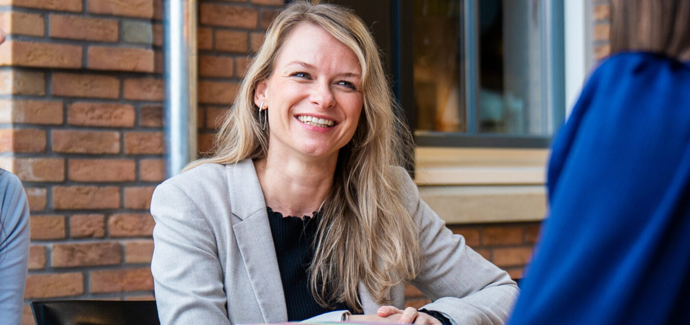 foto van medewerker die lachend aan een tafel zit met een stapel boeken voor zich