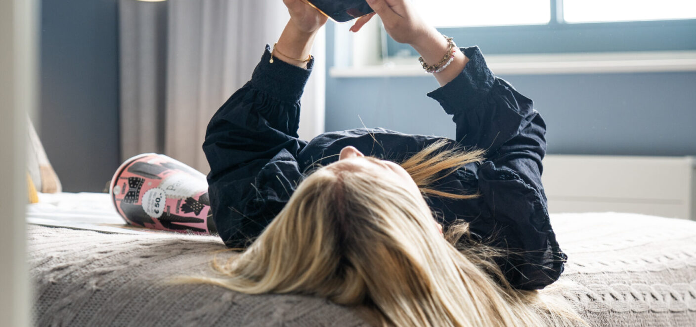 Foto van jonge vrouw liggend op bed met haar telefoon