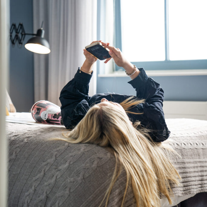 Foto van jonge vrouw liggend op bed met haar telefoon